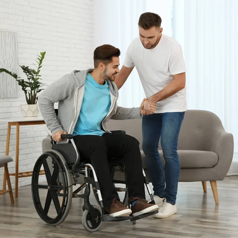 Support worker assisting man to get up from wheelchair